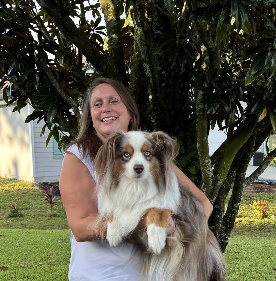 Michelle Martin on her lawn holding a fluffy blue-eyed dog.