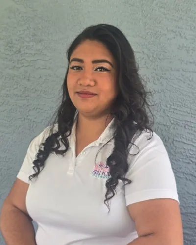 Zainab Osman in a white Mrs. Marvelous Cleaning polo, standing in front of a gray wall.
