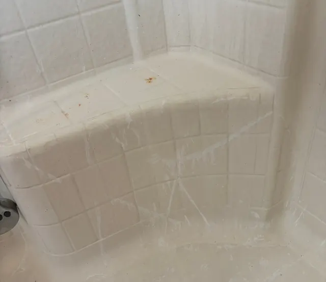 Before: A shower corner seat with rust-coloured stains.